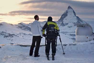 Person with exoskeleton on skis with escort in front of Matterhorn