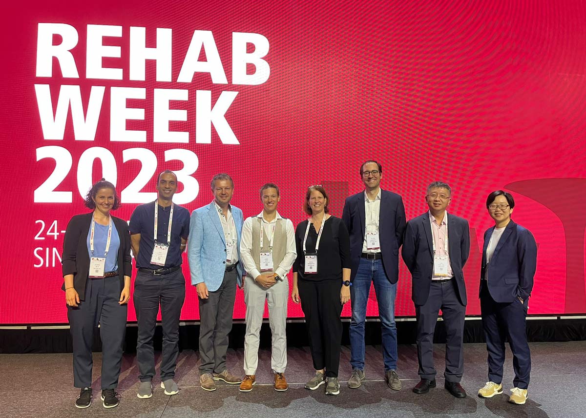Enlarged view: Eight scientists posing in front of a huge display at REHAB Week 2023