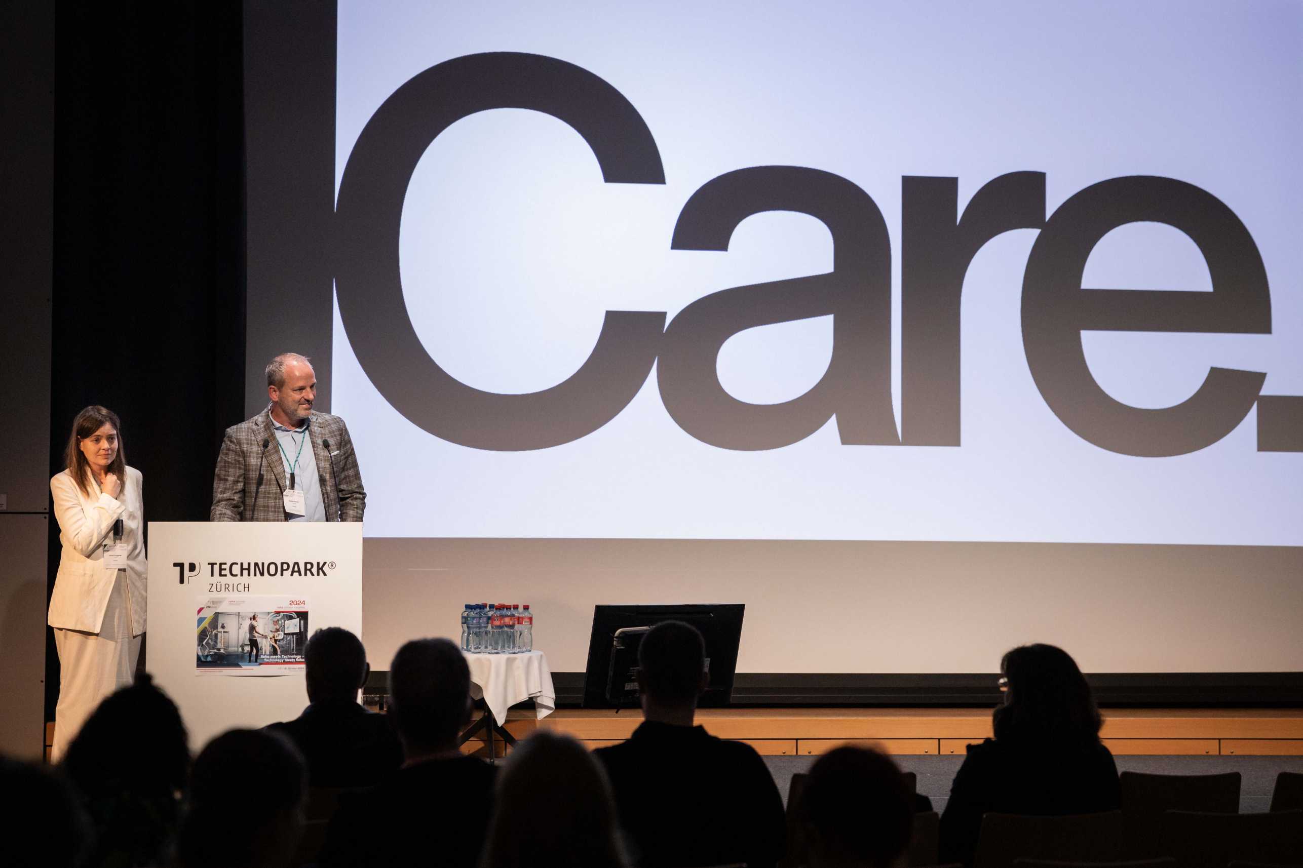 Enlarged view: Two speaker in front of a huge word "care" at symposium