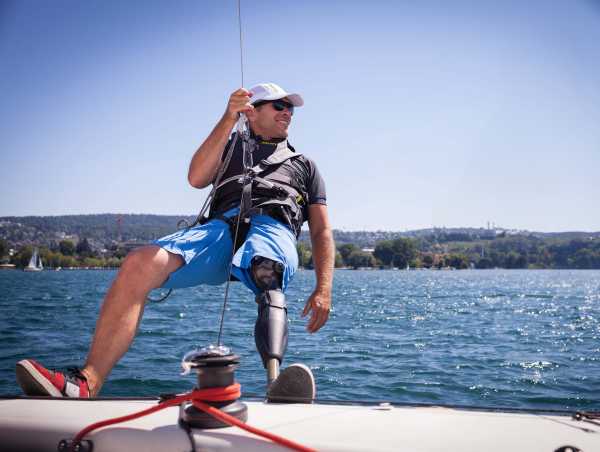 Filip Pockelé with prosthetic leg hangs sideways from sailboat in trapeze