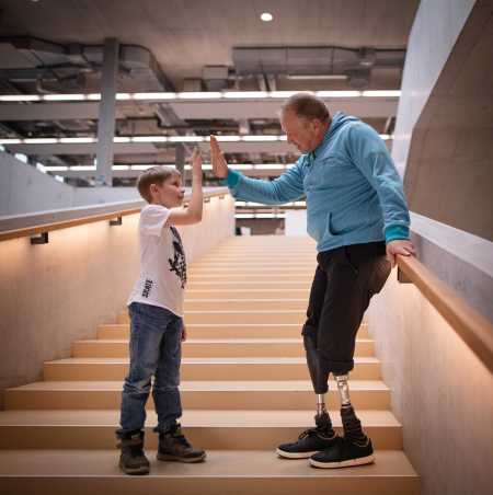 Enlarged view: Rüdiger Böhm with two prosthetic legs poses on long staircase handclap with boy