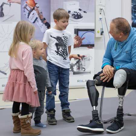 Enlarged view: Rüdiger Böhm with two prosthetic legs talks to 3 children who look at his legs with fascination
