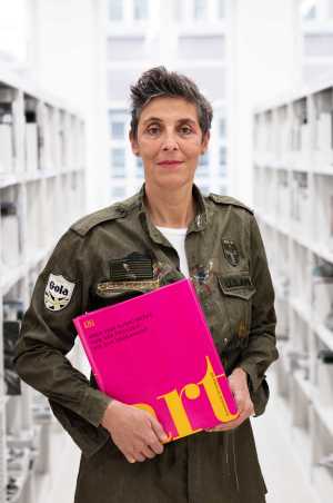 Sibylle Rau stands in the library and holds a book