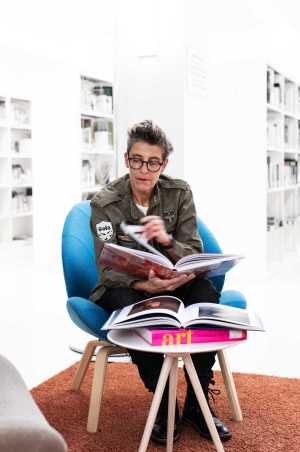 Sibylle Rau sits in an armchair in the library and browses through a book